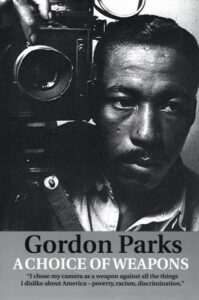 Gordon Parks with camera, text reads "A Choice of Weapons" with quote "I chose my camera as a weapon against all the things I dislike about America -- poverty, racism, discrimination."